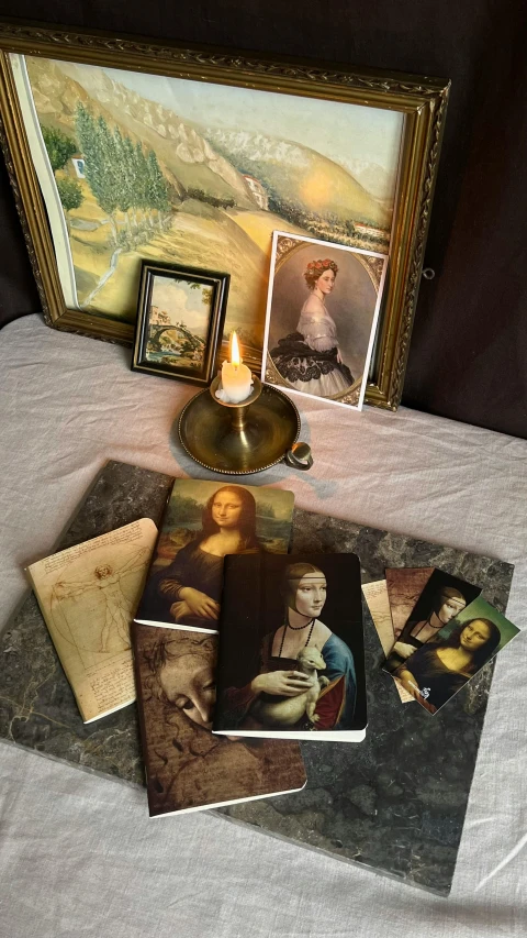 various art pieces are on a white sheet near a candle and a painting