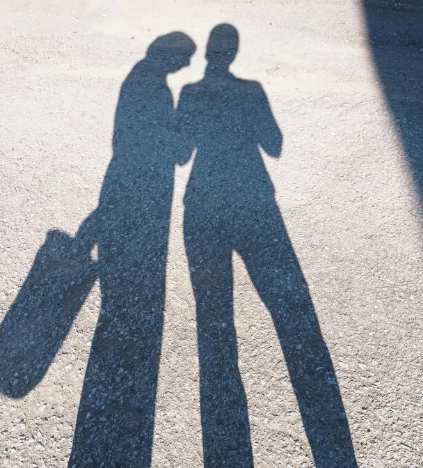 the shadow of two people, one holding a suitcase, are casting a long shadow on a cement surface