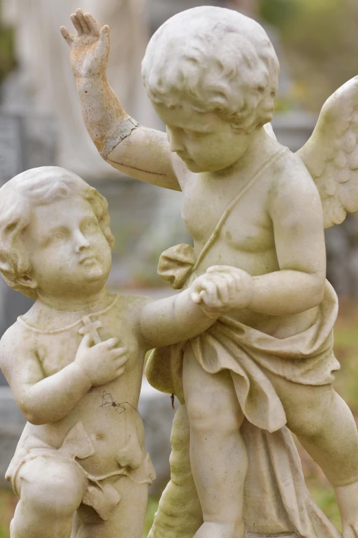 two marble cherub statues holding hands in an old cemetery