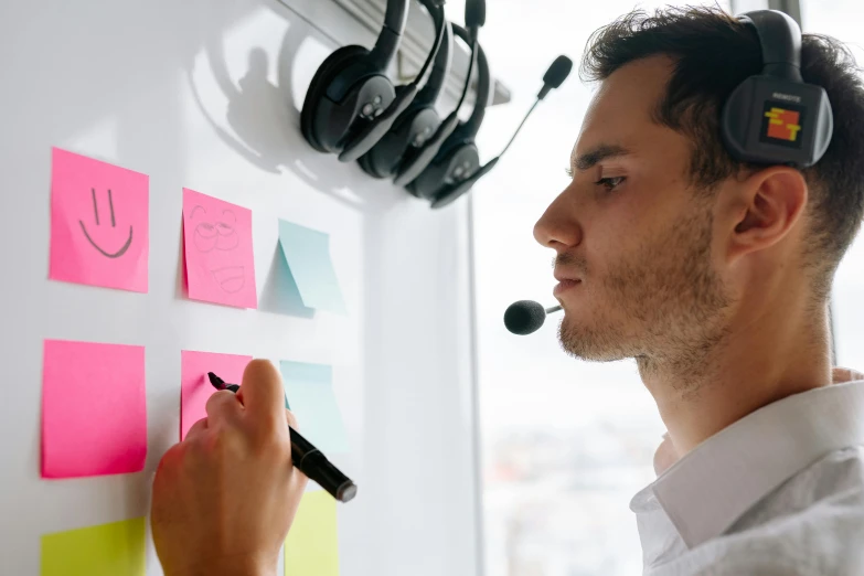 a man with headset on a post - it with different notes and pegs