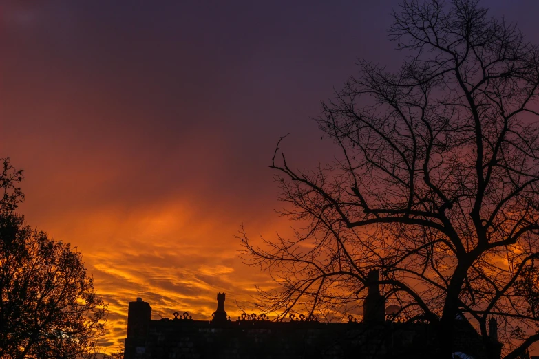 the setting sun is behind a tall building and trees