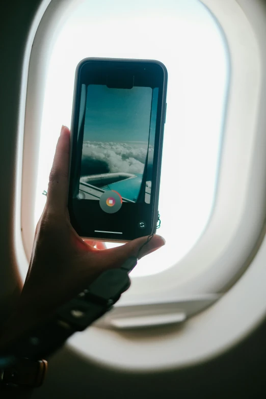 the hand is holding a cell phone next to an airplane window