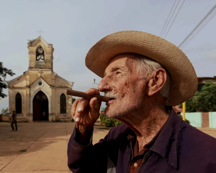 a man with hat holding a cigarette in front of a church