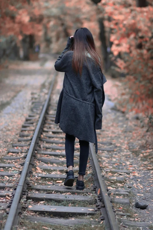 a woman walking down the railroad tracks in the woods