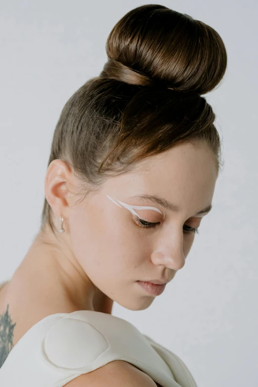 a young woman wearing a white top and hair in a bun