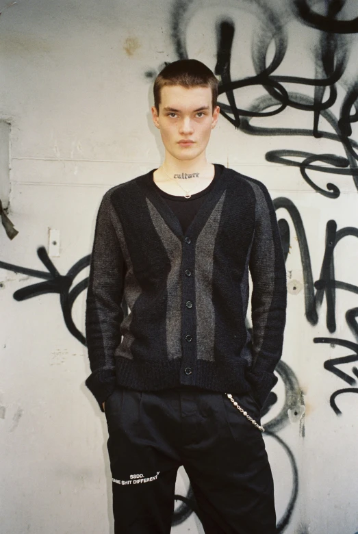 a young man standing in front of a wall covered in graffiti