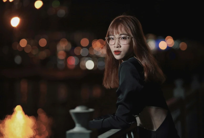 a girl with glasses standing next to a city sidewalk at night