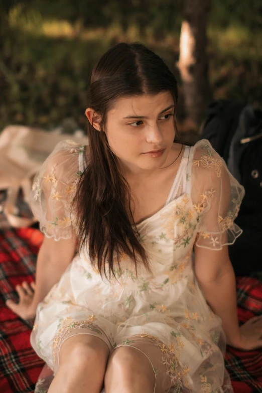 a woman sitting on a bed wearing a white dress and holding an apple in her hand