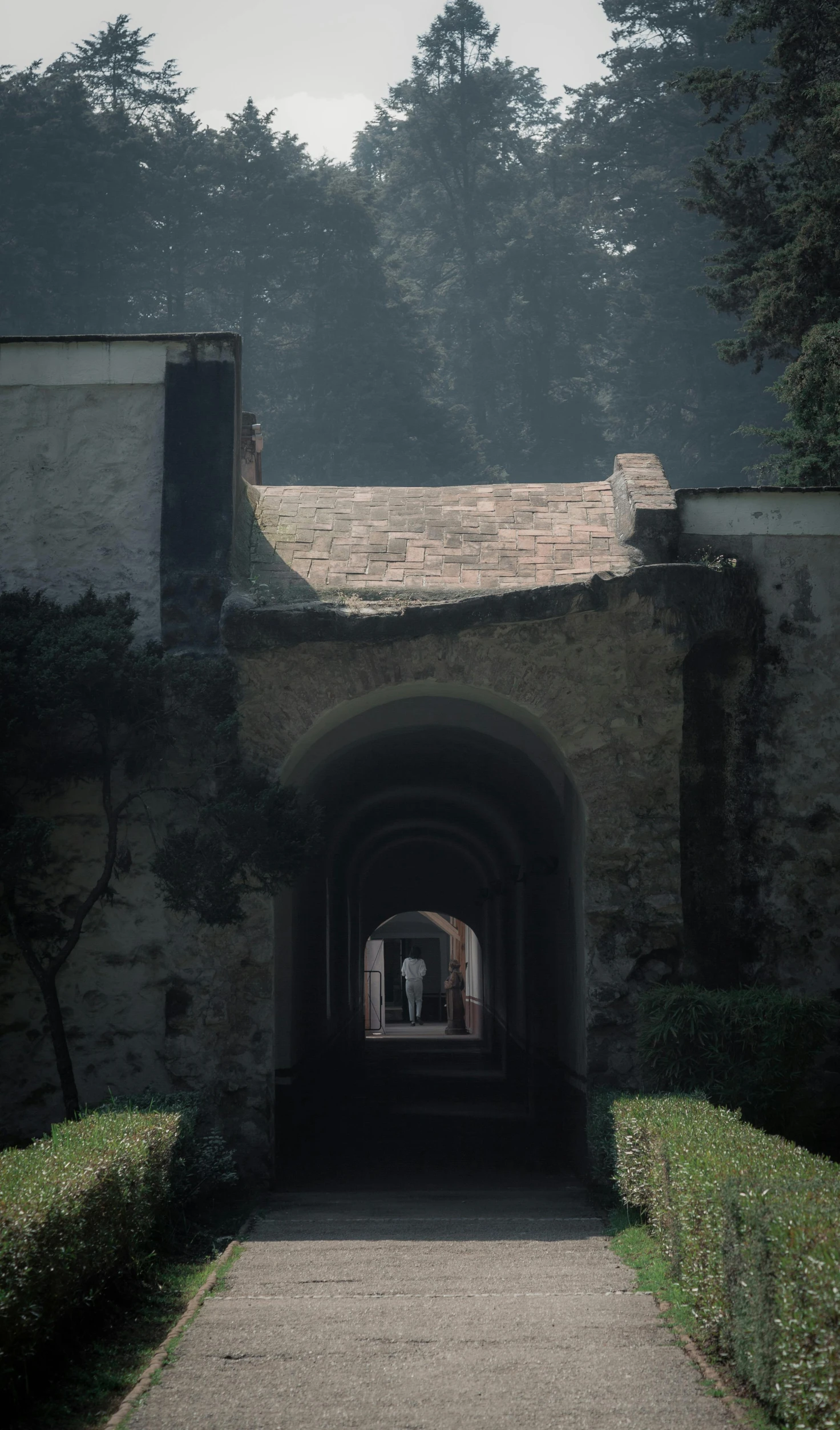 the path through an arched stone building has hedges on either side