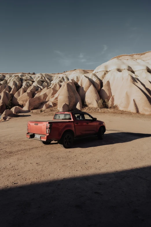 an old red car sits in front of large, jagged rocks