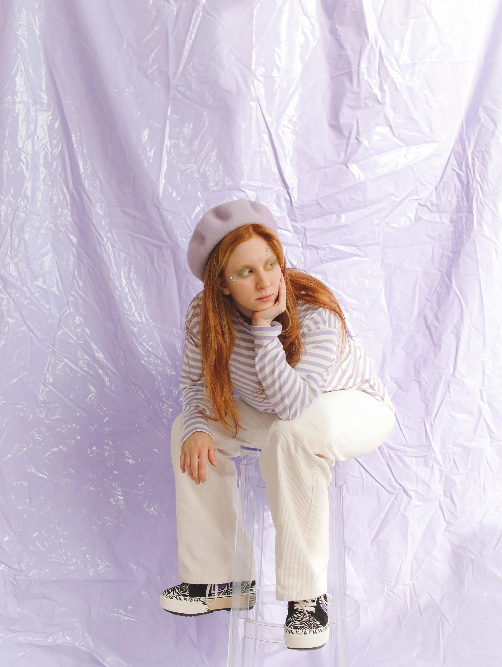 a red - haired girl sits on a stool against a purple background