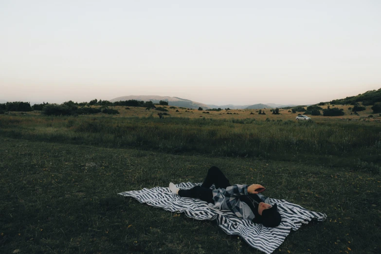 a person is lying on a blanket in a grassy field
