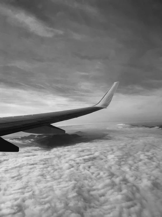 an airplane wing flies above the clouds in black and white