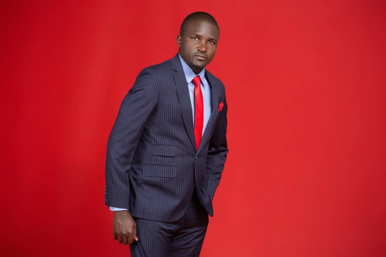 a man in a suit stands against a red background