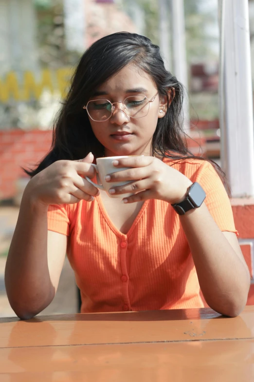 a woman with glasses sitting at a table looking down at her cell phone