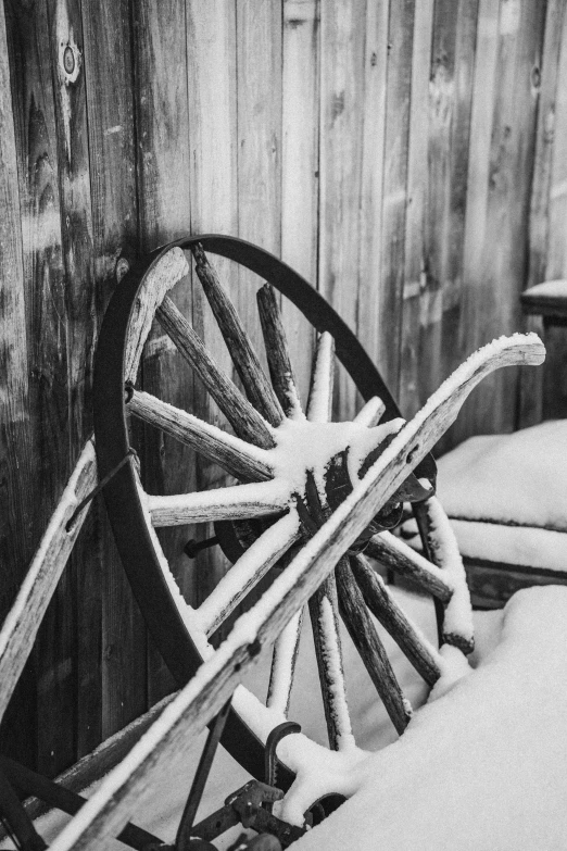 an old wagon with snow on the rim sitting in front of a fence