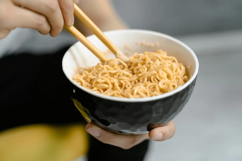 a person holding a black bowl of noodles and chop sticks