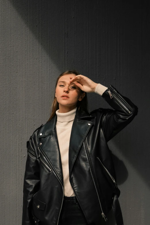 a woman poses in a leather jacket while wearing a turtle neck sweater