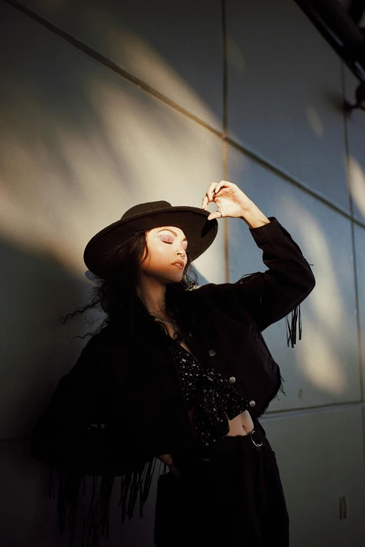 woman in black dress and black hat standing against a wall