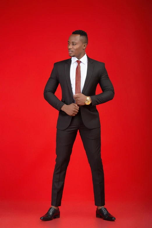 a man in a black suit posing with a red background