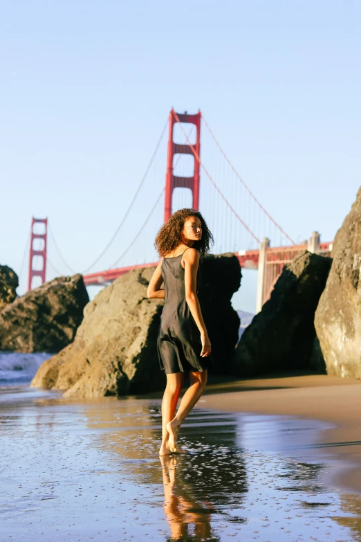 a beautiful woman walking along the beach near the golden gate bridge