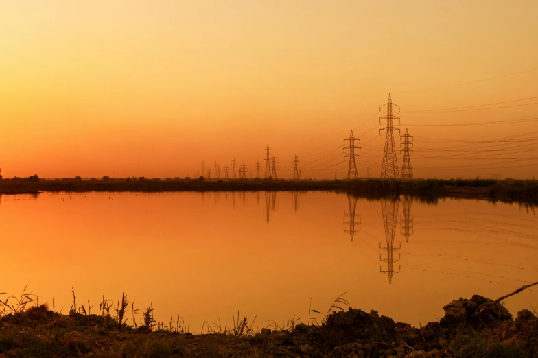 the sun rising over a lake and power lines