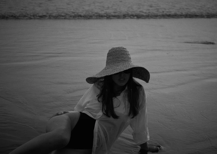 a girl sitting on the beach with her hat on