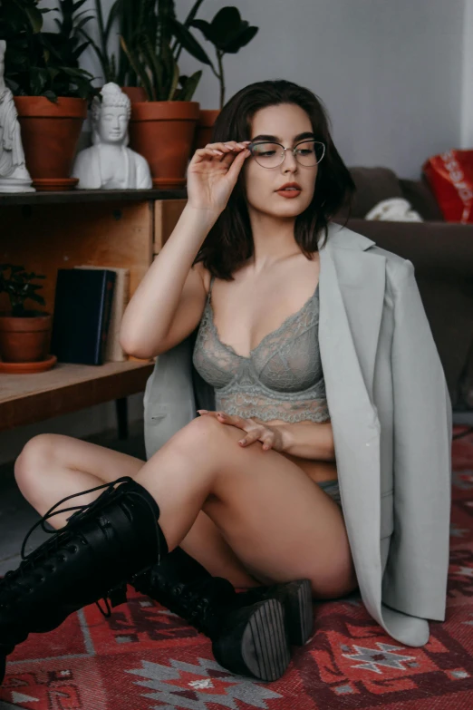 a woman with glasses and short shorts sits on a bed in lingerie