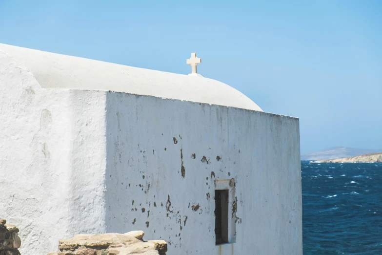 a white building with a cross above it on the edge of the water