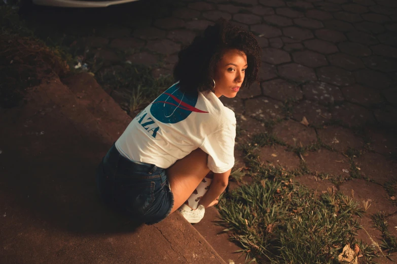 a woman is sitting on the sidewalk with her hands behind her back