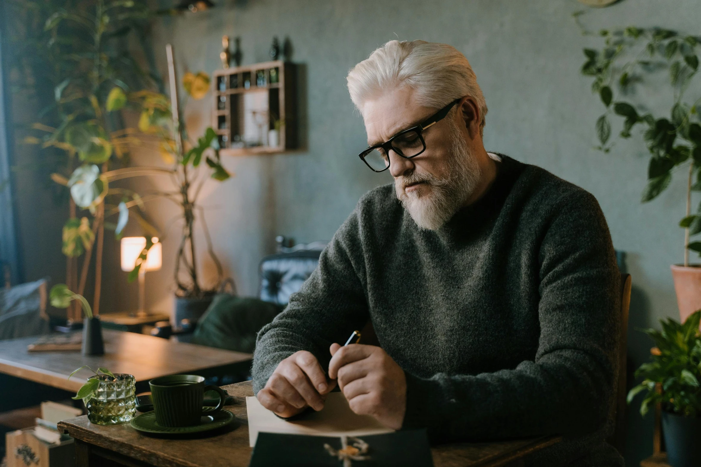 an old man sits at his desk while holding a pen and writing