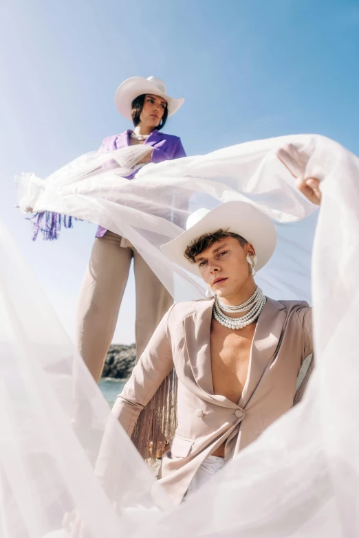 two women wearing white clothes and hats stand on the beach