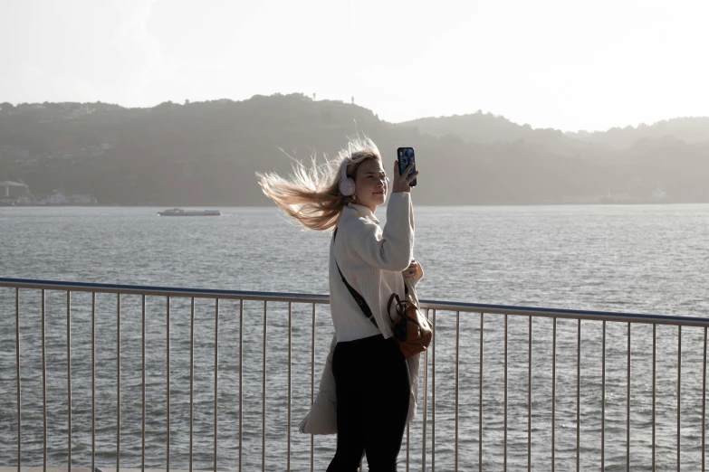 a woman taking a po with her cell phone near a lake