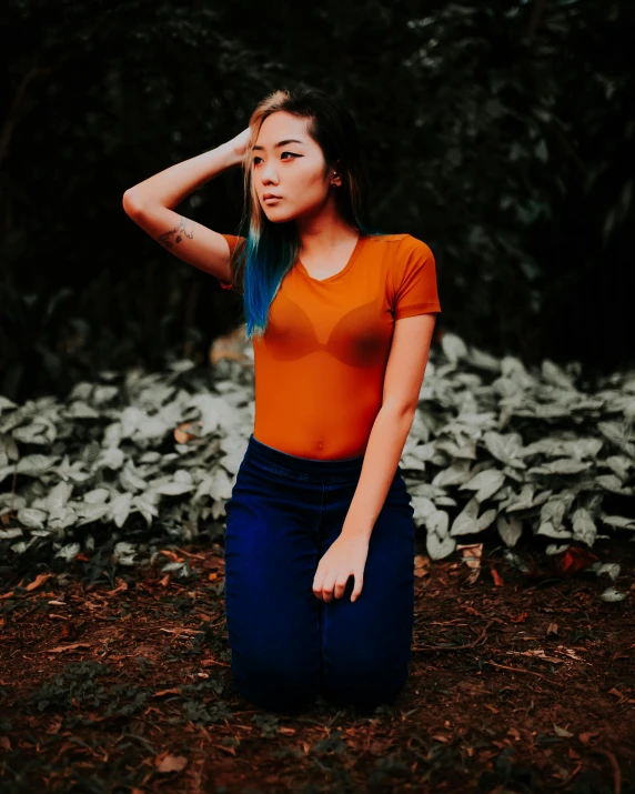 a young lady in an orange top and blue pants sitting outdoors