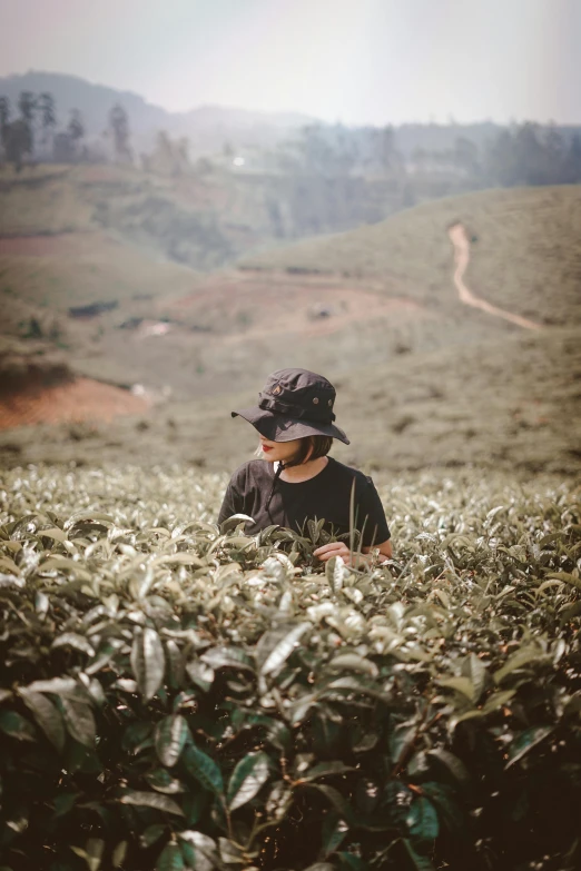 a woman with a hat is sitting in the middle of a green field