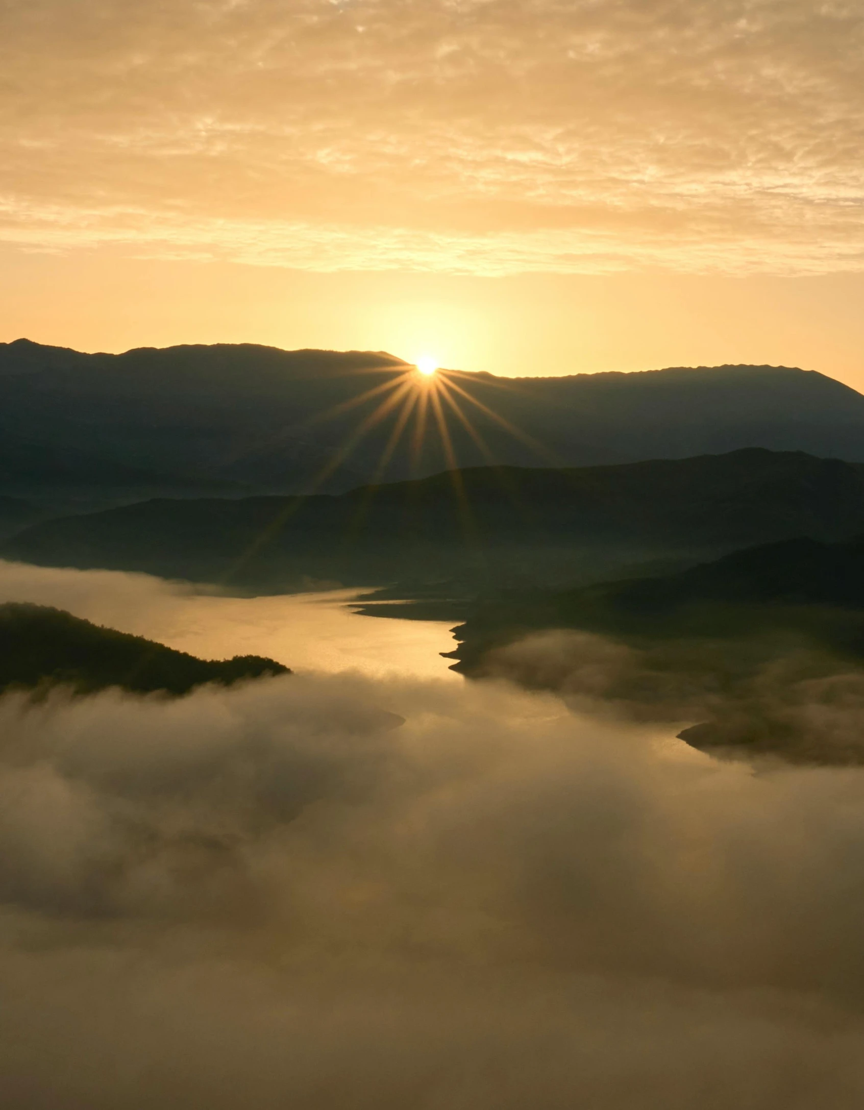 sun set over clouds over mountains and a lake