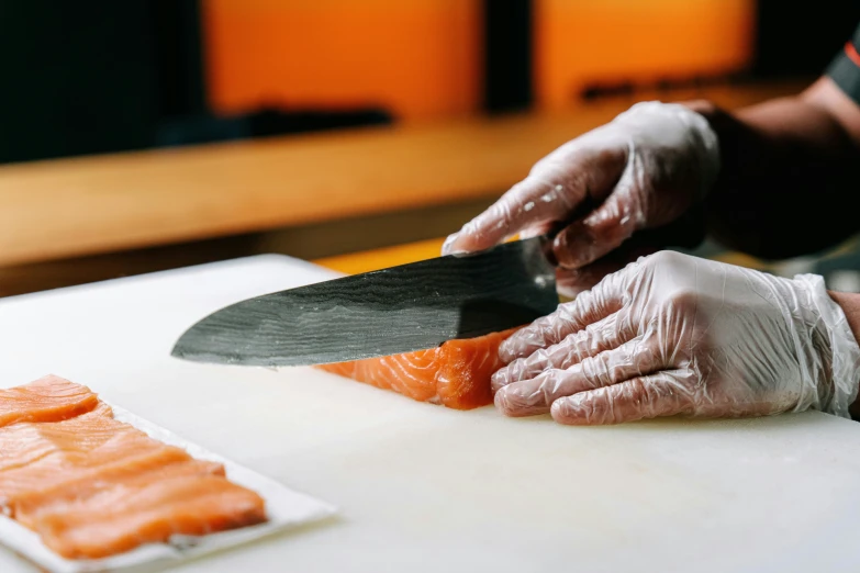 someone in gloves  salmon with a knife on top of a table