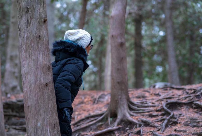 a person in a black jacket leaning against a tree in a forest