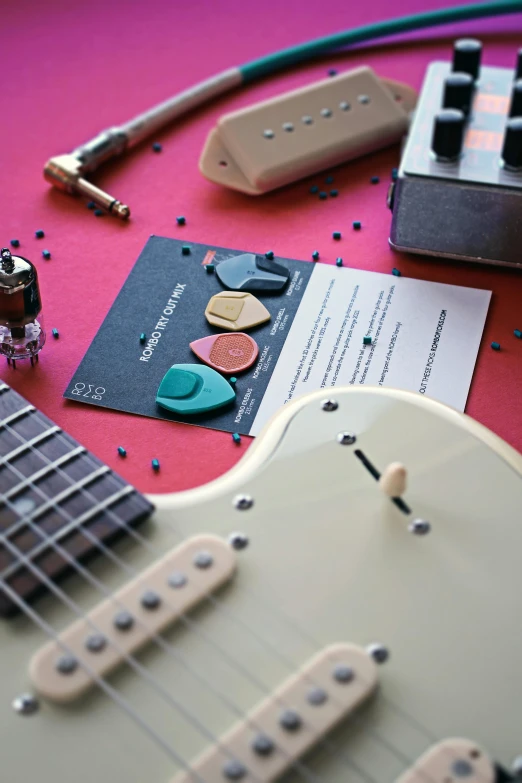 a guitar with a paper guitar picker and other accessories on a pink table