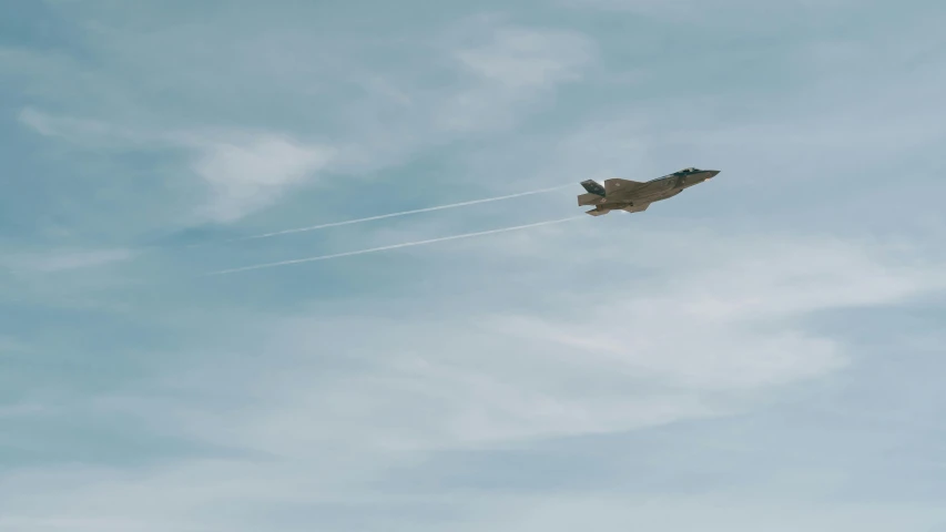 a fighter jet flying through a cloudy blue sky