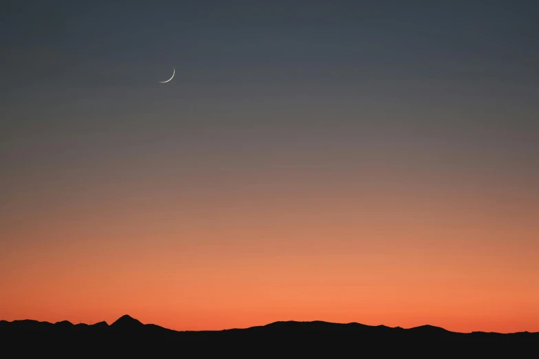 the moon over mountains silhouetted against a sky