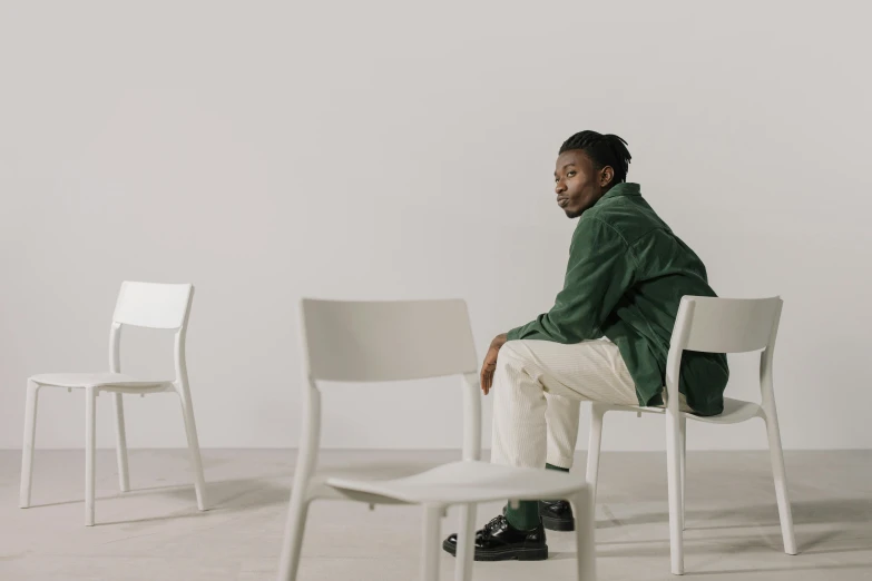 a black man sits on a white chair and looks to his left
