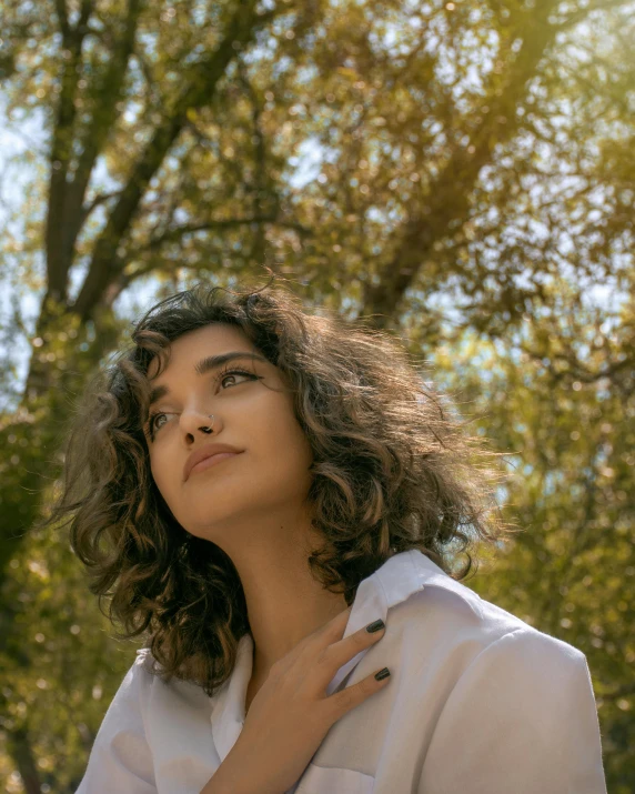 a woman wearing a shirt is posing under some trees