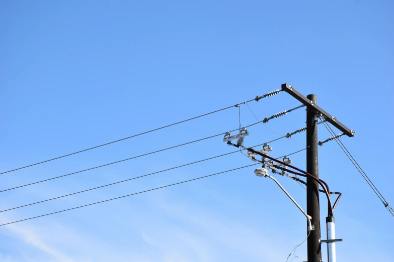 wires and stoplights on a street post with a blue sky behind