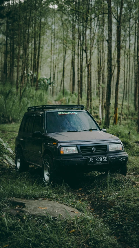 a small black suv in the woods on a trail
