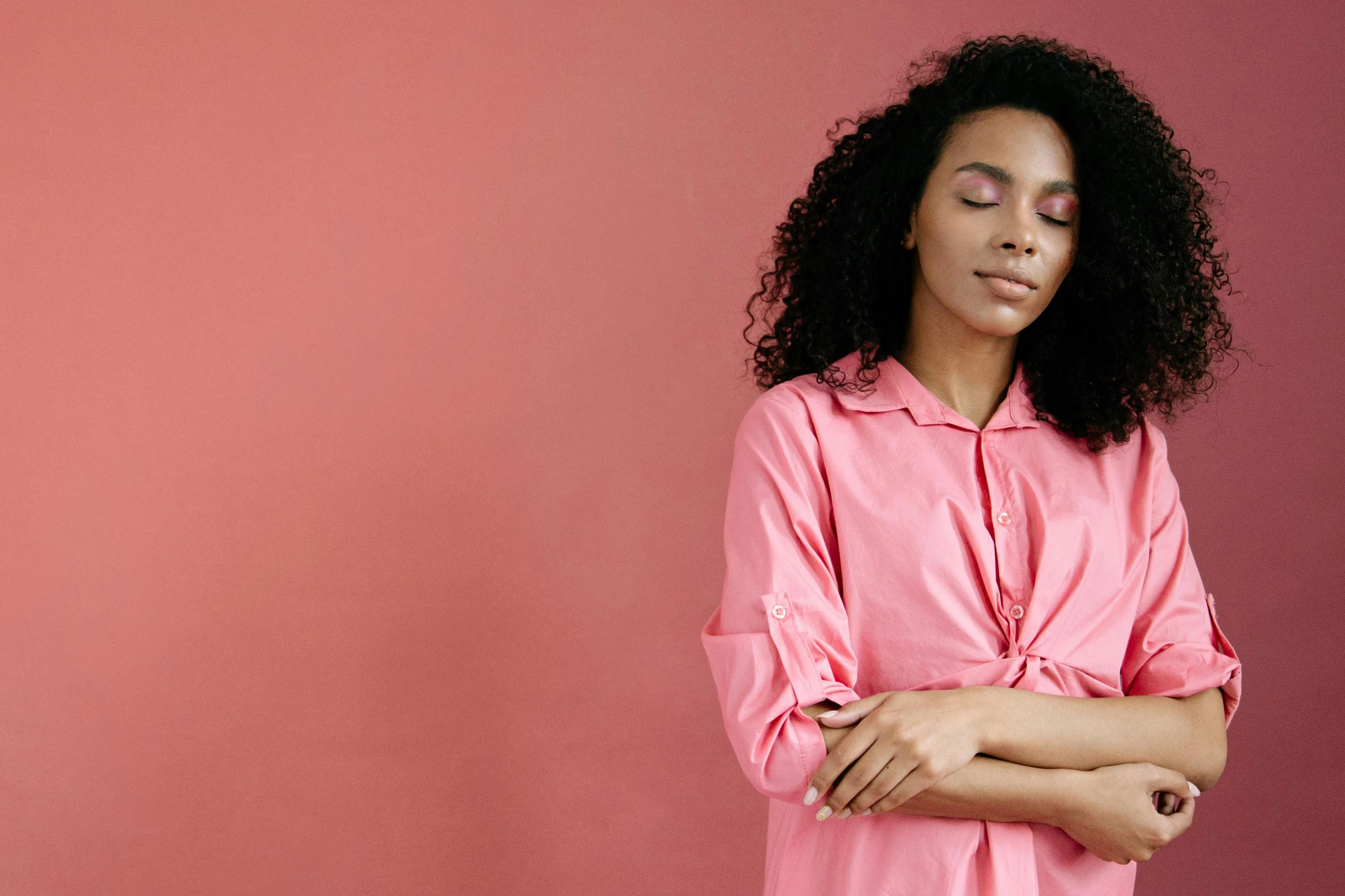 a woman stands with her arms folded while wearing a pink shirt