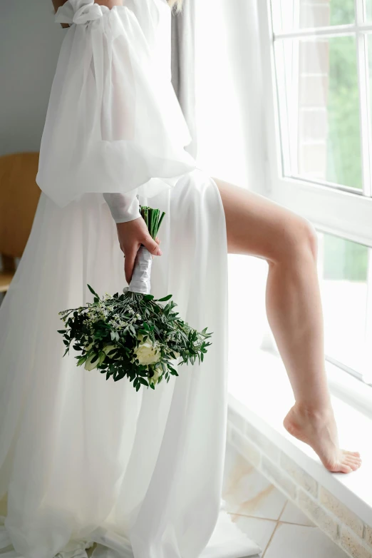 a woman in white dress holding a bouquet of greenery