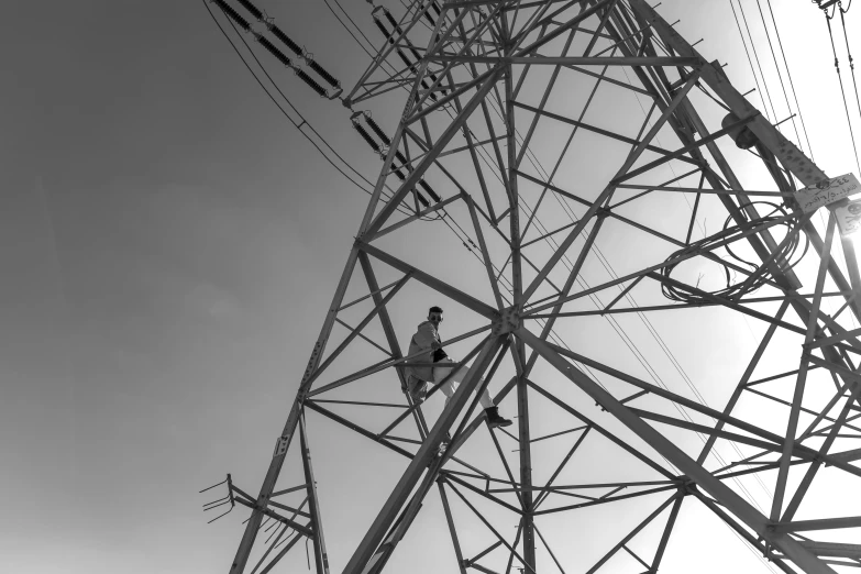 black and white pograph of a worker repairing the top of an electricity tower