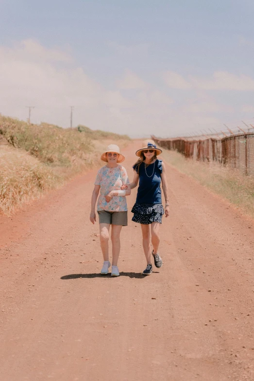 two women are walking down a dirt road together