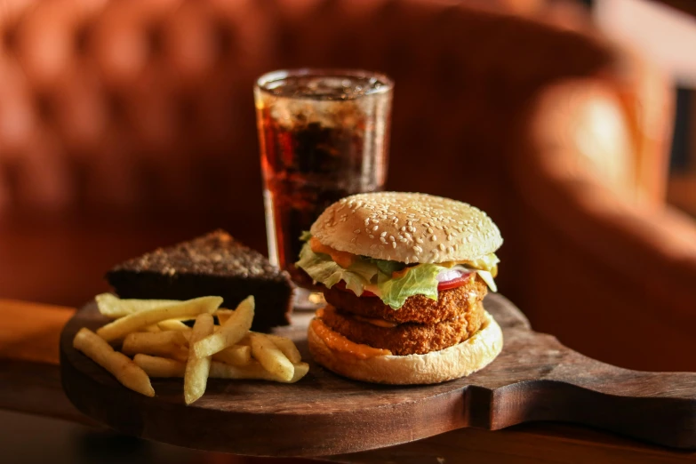 chicken sandwich on top of a wooden tray with french fries and a glass